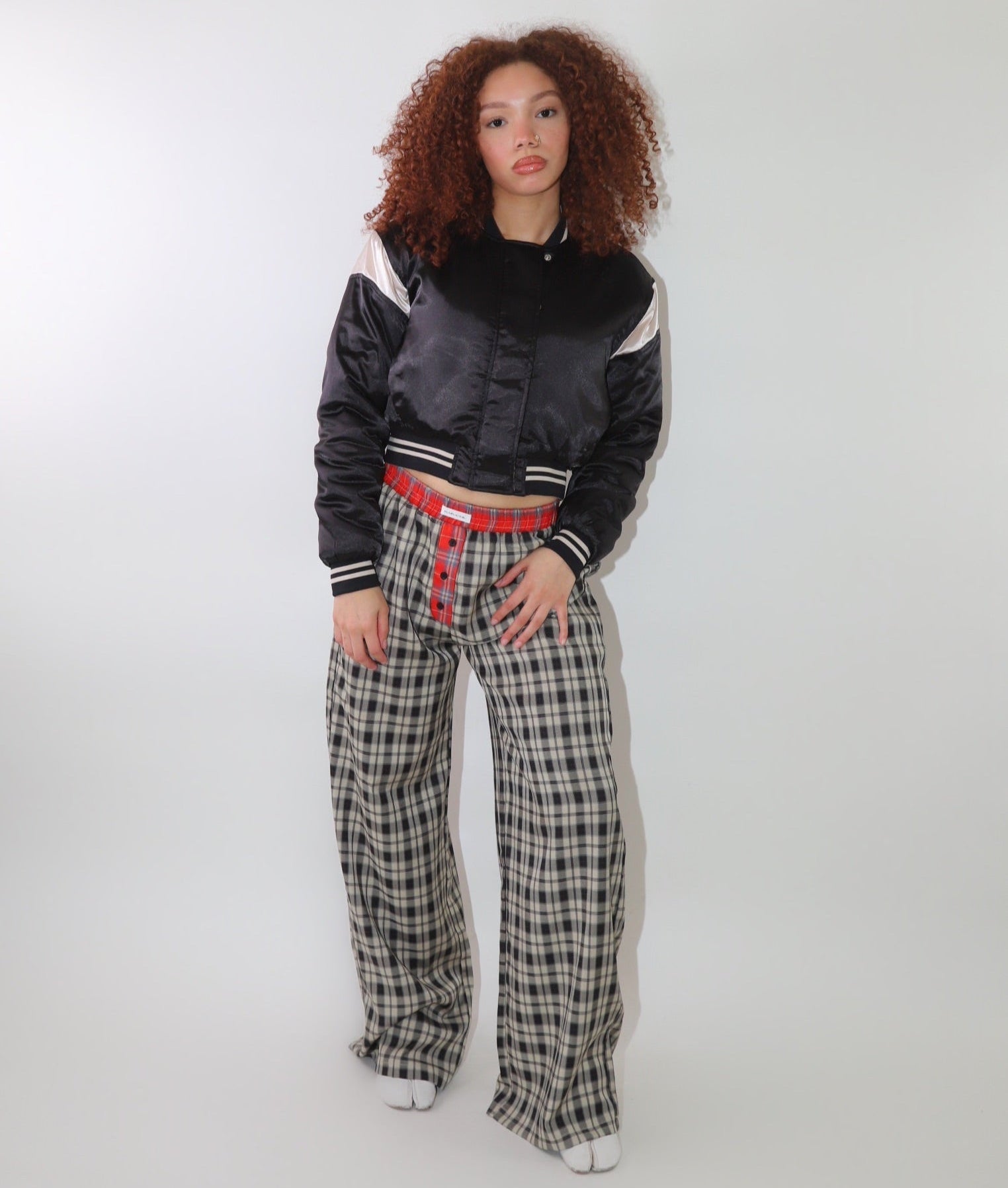 A woman wearing high-waisted cream and black plaid wide-leg pants with a relaxed fit and contrasting black-and-white plaid waistband detail. The pants have an effortless oversized silhouette, making them perfect for cozy yet stylish wear.