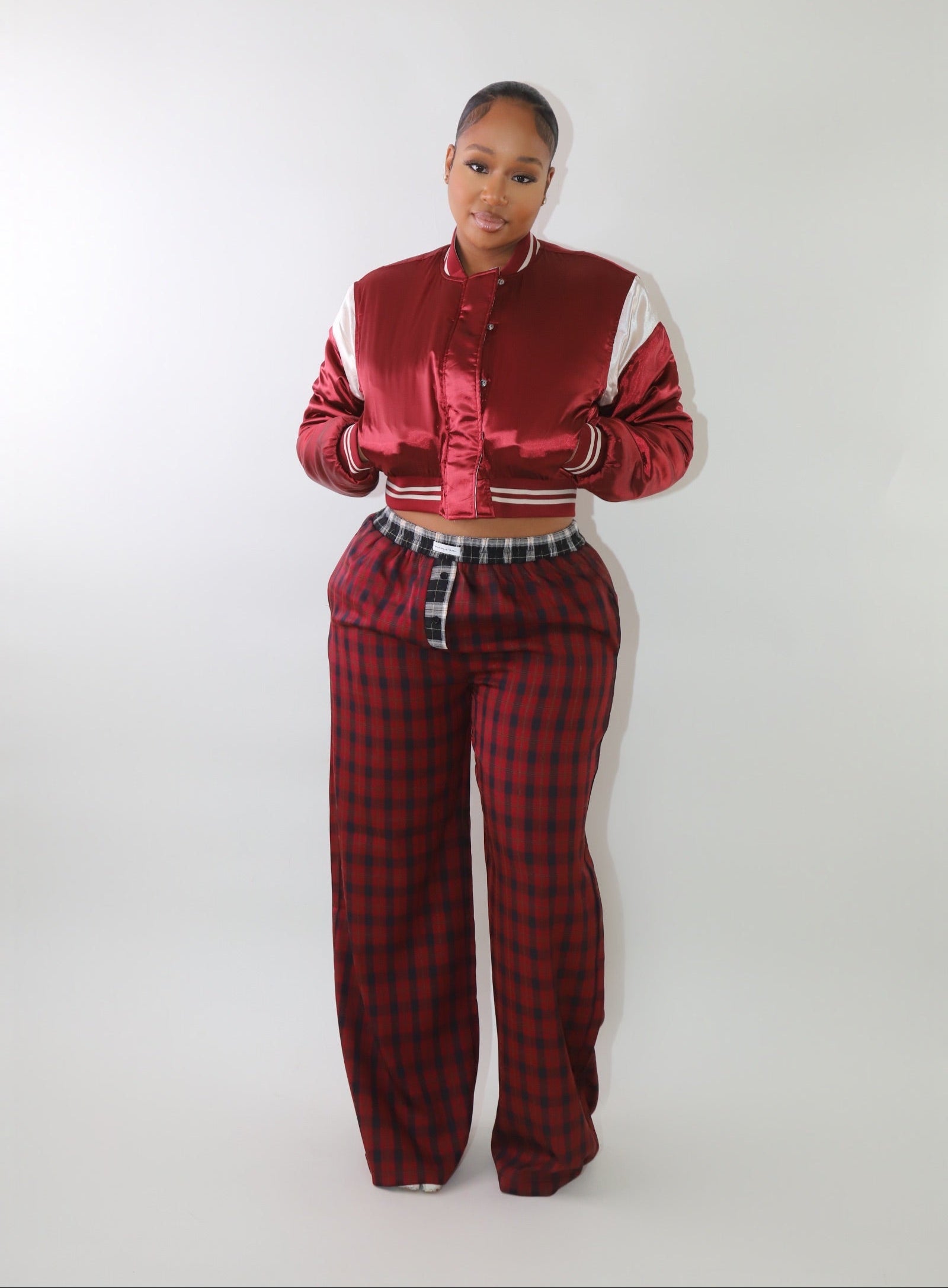 A woman wearing high-waisted red and black plaid wide-leg pants with a relaxed fit and contrasting black-and-white plaid waistband detail. The pants have an effortless oversized silhouette, making them perfect for cozy yet stylish wear.