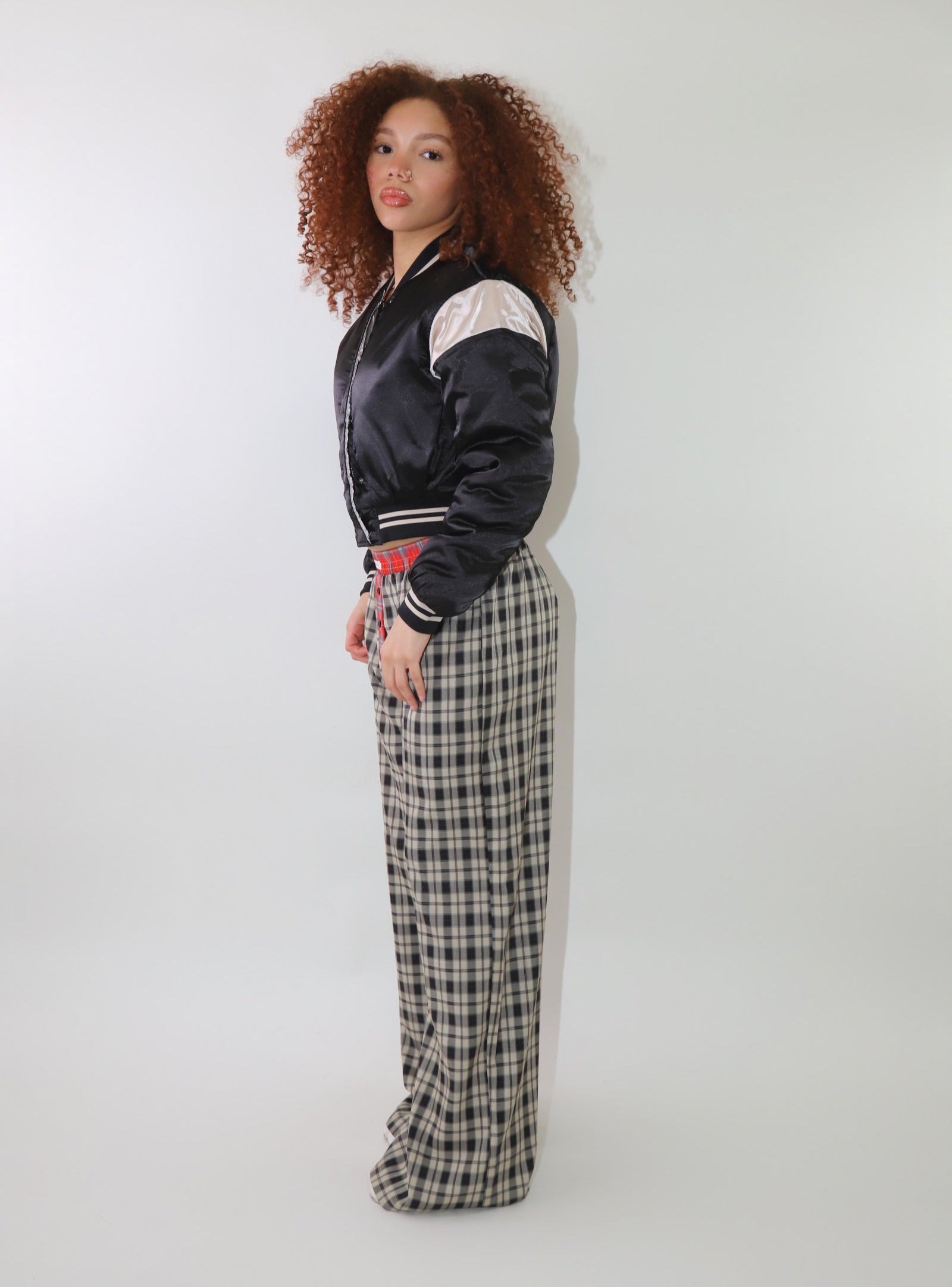 A woman wearing high-waisted cream and black plaid wide-leg pants with a relaxed fit and contrasting black-and-white plaid waistband detail. The pants have an effortless oversized silhouette, making them perfect for cozy yet stylish wear.