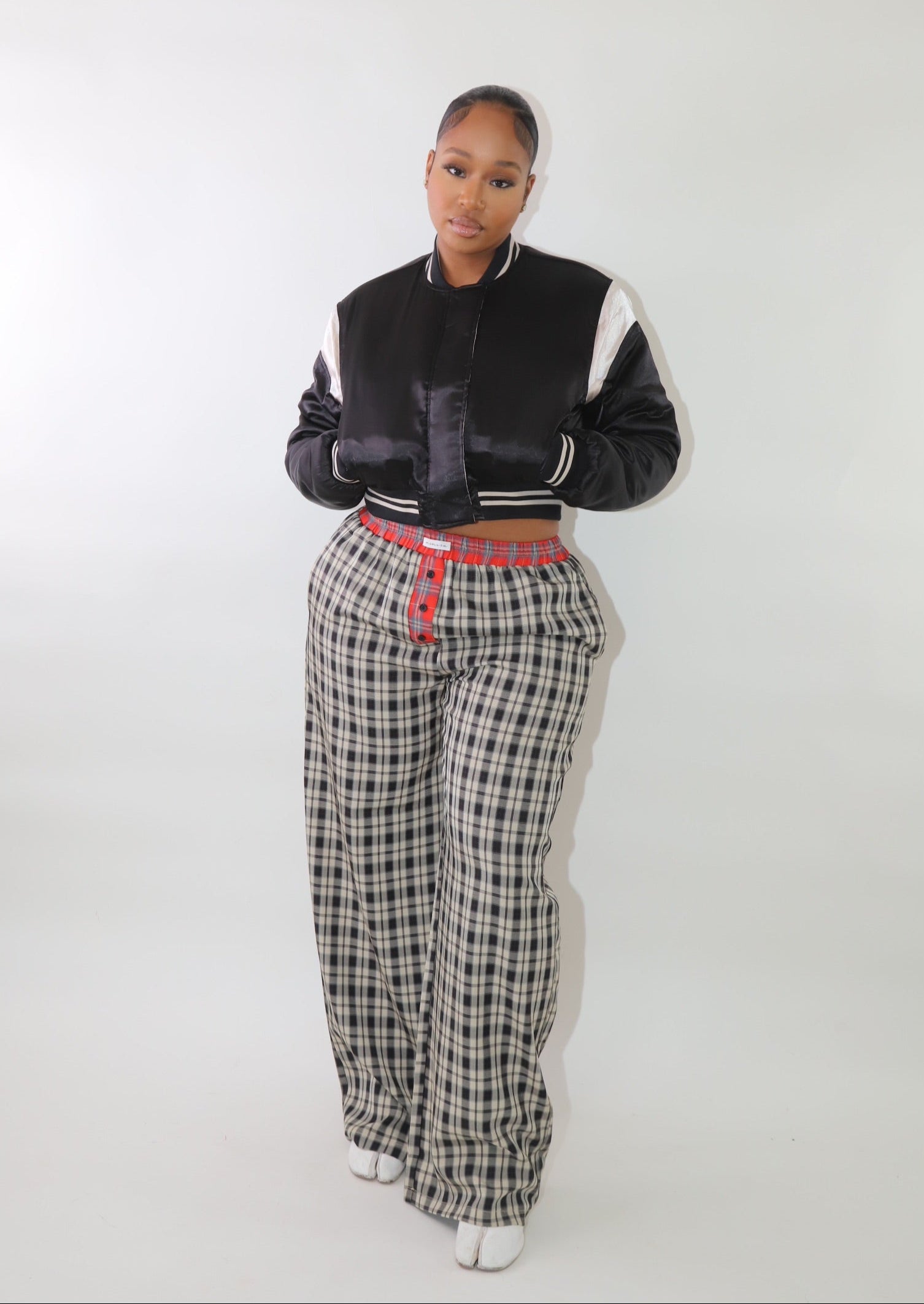 A woman wearing high-waisted cream and black plaid wide-leg pants with a relaxed fit and contrasting black-and-white plaid waistband detail. The pants have an effortless oversized silhouette, making them perfect for cozy yet stylish wear.