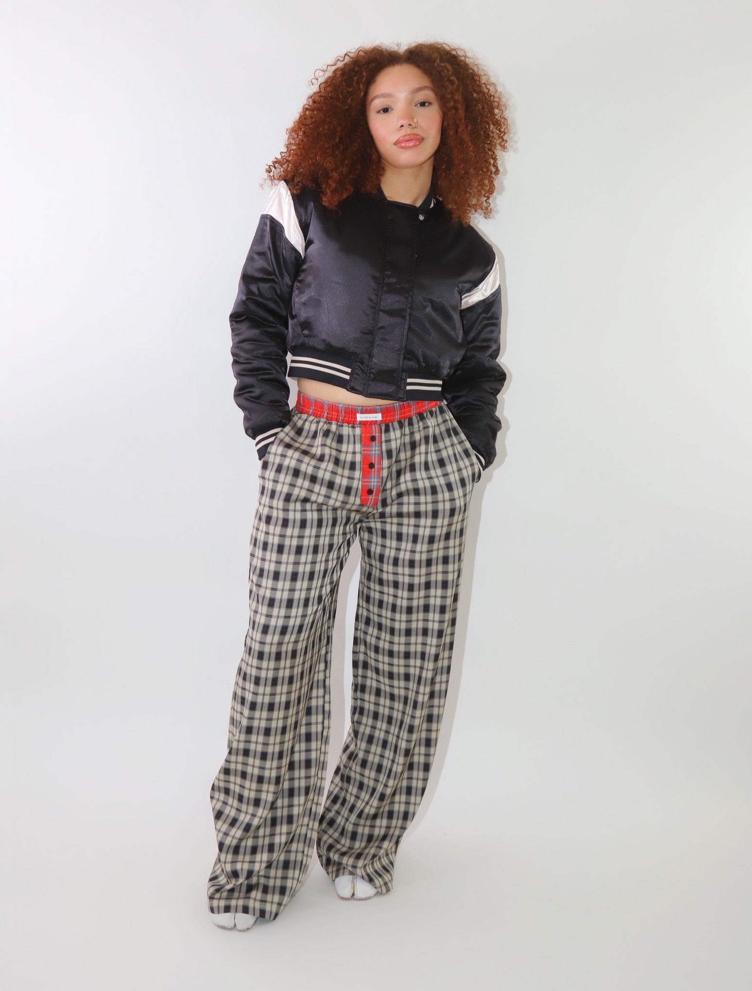 A woman wearing high-waisted cream and black plaid wide-leg pants with a relaxed fit and contrasting black-and-white plaid waistband detail. The pants have an effortless oversized silhouette, making them perfect for cozy yet stylish wear.
