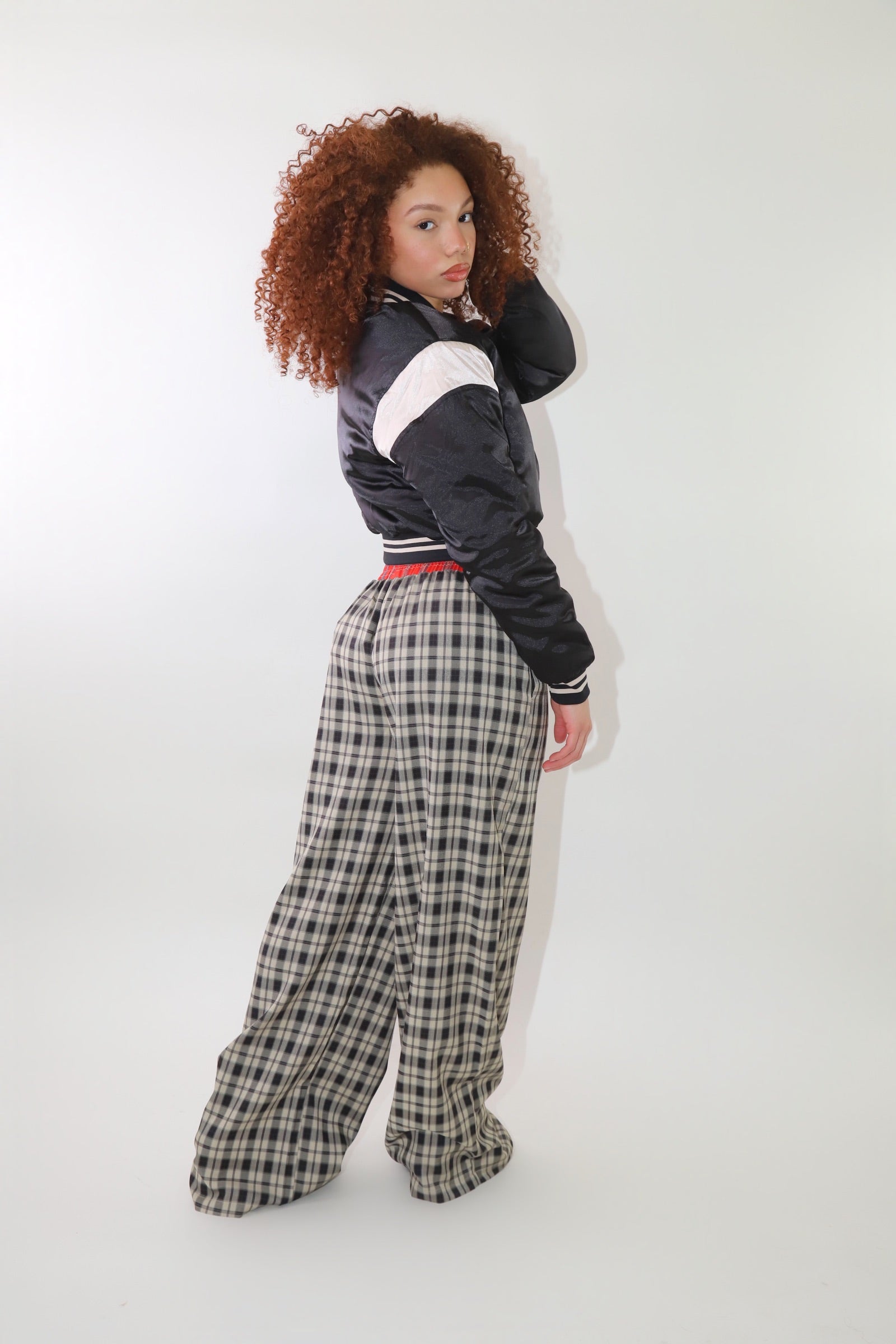 A woman wearing high-waisted cream and black plaid wide-leg pants with a relaxed fit and contrasting black-and-white plaid waistband detail. The pants have an effortless oversized silhouette, making them perfect for cozy yet stylish wear.