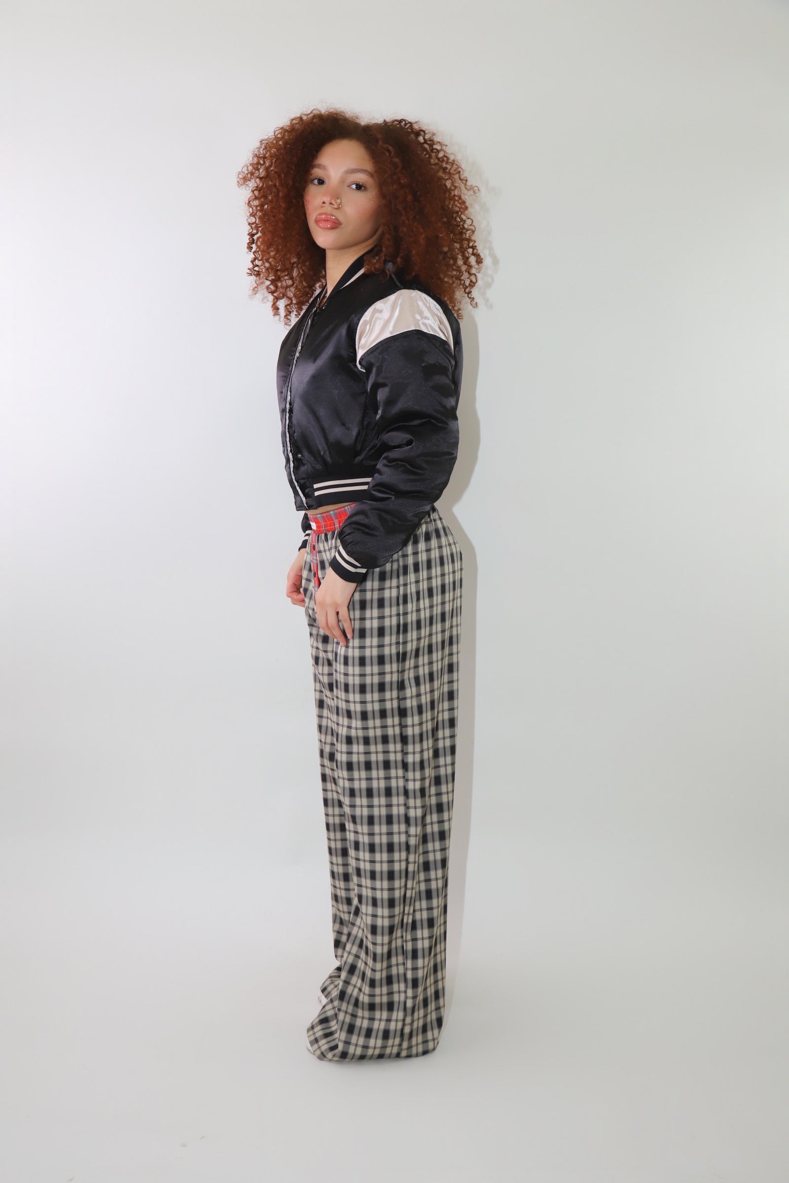 A woman wearing high-waisted cream and black plaid wide-leg pants with a relaxed fit and contrasting black-and-white plaid waistband detail. The pants have an effortless oversized silhouette, making them perfect for cozy yet stylish wear.