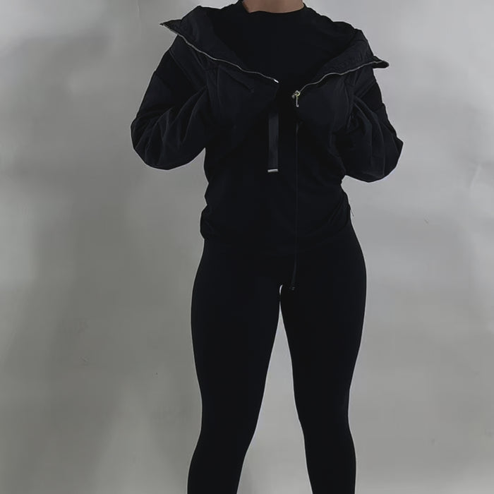 video Woman with curly red hair wearing a brown cropped puffer jacket over a matching brown fitted outfit, posing with hands on the jacket collar against a plain white background. Trendy and cozy outerwear loo