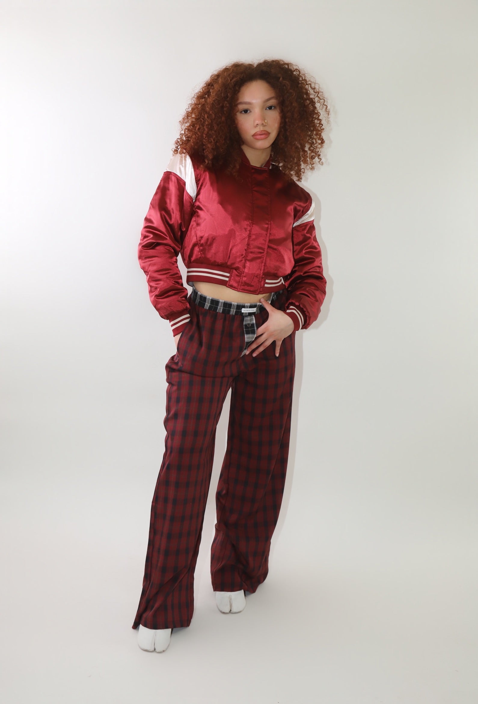 A woman wearing high-waisted red and black plaid wide-leg pants with a relaxed fit and contrasting black-and-white plaid waistband detail. The pants have an effortless oversized silhouette, making them perfect for cozy yet stylish wear.
